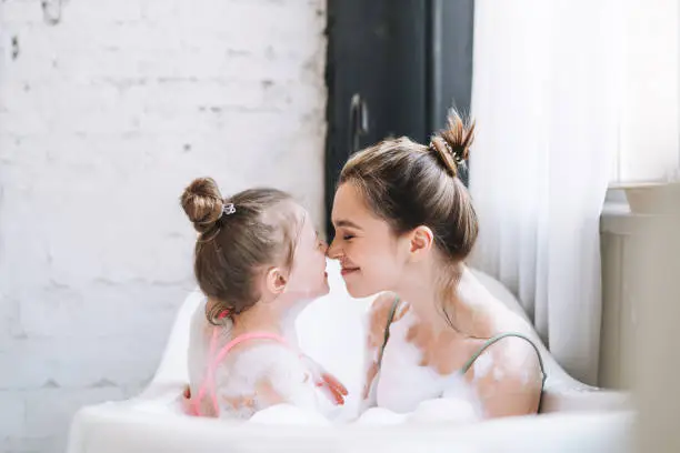 Photo of Young mother woman and little tween girl daughter having fun in bath with foam at home