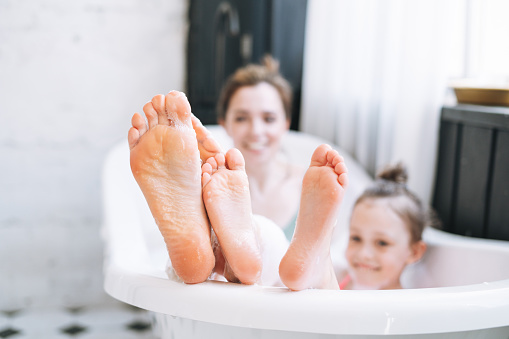 Young mother woman and little tween girl daughter having fun in bath with foam at home