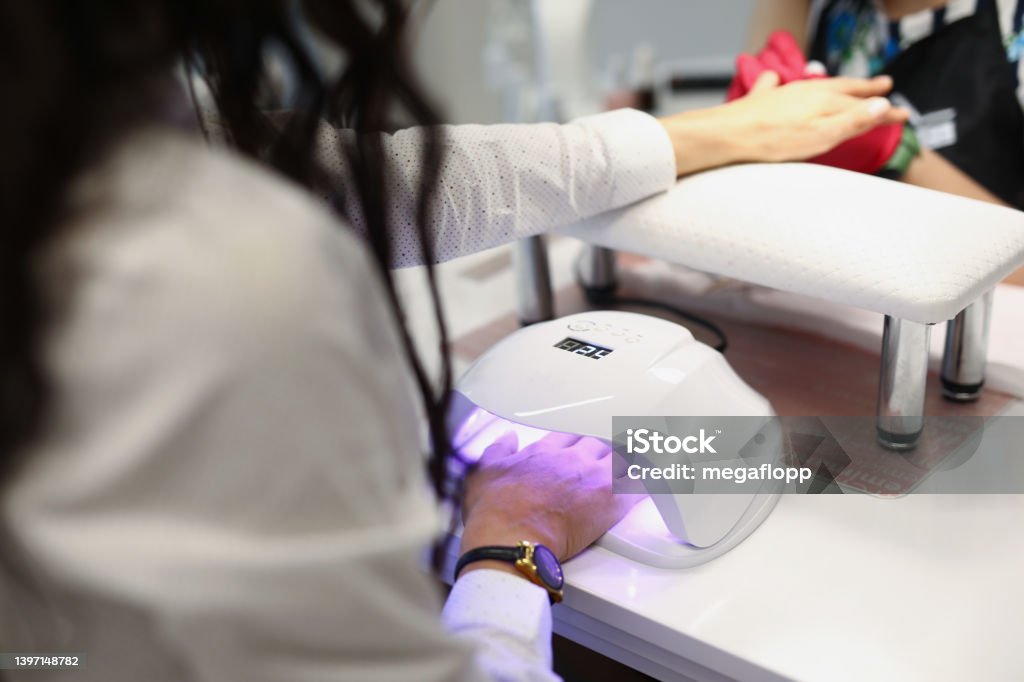 Lady drying gel in ultraviolet lamp Close-up of manicurist covering nails of client with lights nail polish. Businesswoman preparing to meeting with colleagues. Beauty salon and personal care concept Manicure Stock Photo