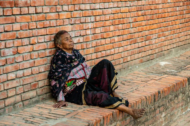 Bhaktapur, Nepal - oct 28, 2019: an elderly Nepalese woman is resting on a small wall of bricks at Durbar Square in Bhaktapur, Nepal
