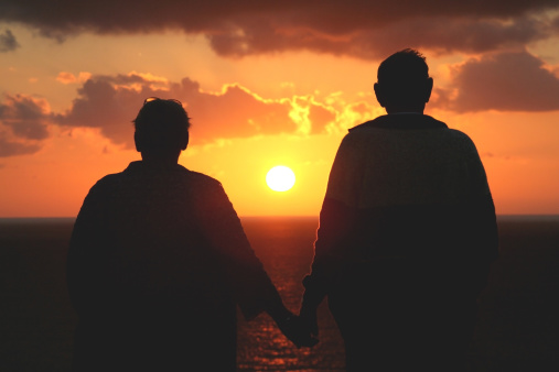 Older couple watching the sunset. Standing hand in hand.