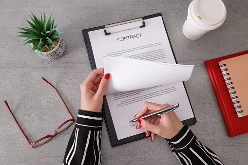 Close up of a businesswoman hand signing a contract on a desk at office.