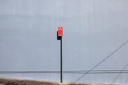 Red metal No stopping sign on a gray metal pole, with a wall behind.