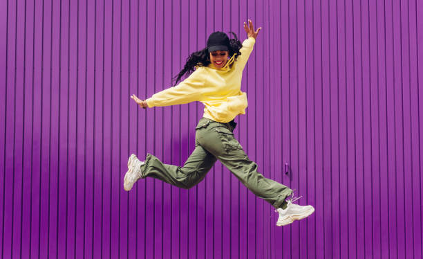 Jumping young woman in yellow dress on purple background. Dancer of hip hop and trap music. Concept of freedom, celebration, joy. Jumping young woman in yellow dress on purple background. Dancer of hip hop and trap music. Concept of freedom, celebration, joy. pop music stock pictures, royalty-free photos & images
