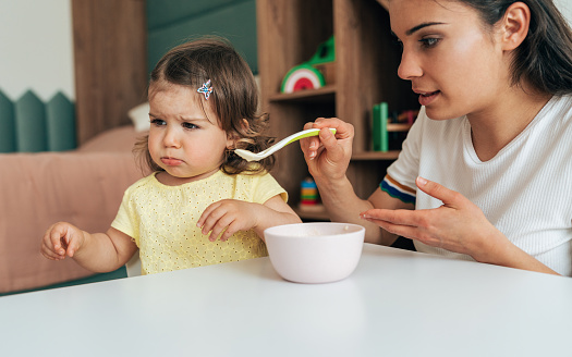 Young mother feeding her baby girl with a spoon at home
