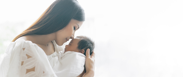 Panoramic banner image of beautiful young Asian mother kissing and hugging newborn baby. Beautiful Family. Maternity concept. Parenthood. Motherhood, adoption concept