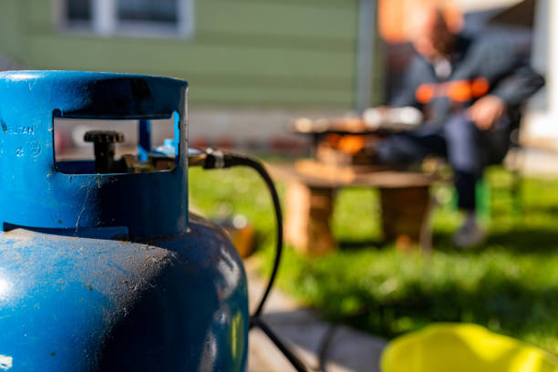 Unrecognizable man making barbecue with gas stove in a backyard, focus is on gas bottle