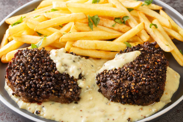 Classic French dish steak au poivre is a filet mignon with a crunchy peppercorn crust and rich Cognac sauce served with french fries close-up in a plate. horizontal