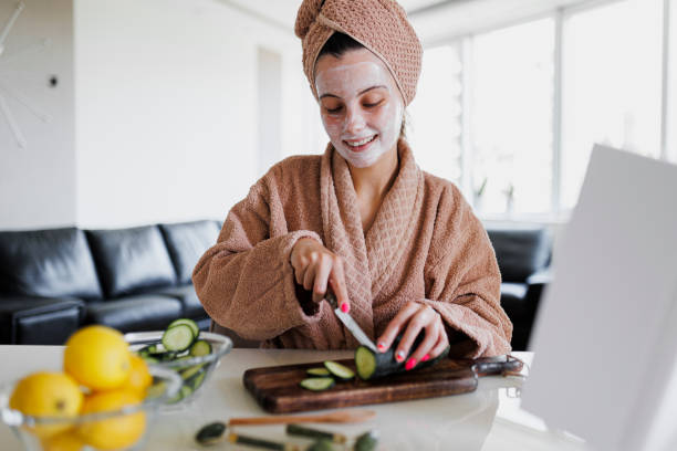 Smiling woman cutting cucumber and making face mask, Portrait of young woman applying face mask at home. Natural Skin Care Routine For Glowing Skin. Woman at home having skin care routine. Concept of natural cosmetics skin care mujer sonriente cortando pepino y haciendo mascarilla, retrato de mujer joven aplicándose mascarilla en casa. rutina natural de cuidado de la piel para una piel brillante. mujer en casa con rutina de cuidado de la piel. concepto de cosmética natural cuid
