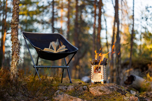 Camping chair with a book, burning wood stove in the forest. Stove in focus, background blurred selective focus. stock photo