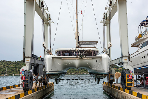 Crane lifting a sailboat (catamaran) above the water on the dock for maintenance in Kaş Marina, Antalya.