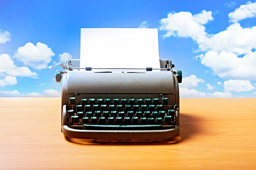 Typewriter on wooden desk with idyllic sky behind it.