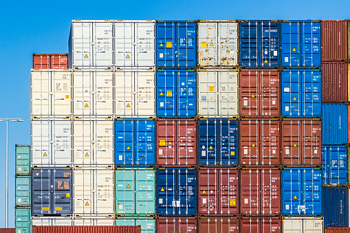 End view stack of colourful steel shipping containers in port showing door panels & locking mechanisms plus some fixed end panels. Identification logos and codes edited with some unidentifiable data retained for context. Fremantle Port.