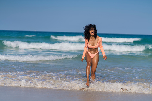 Afro Latin woman of average age of 30 years dressed in a salmon colored bikini is on vacation at the beach enjoying the sun and the breeze