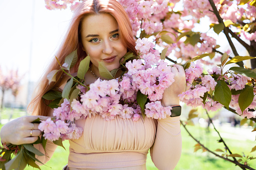 Hipster woman near sakura blooming tree. Pink flowers, spring and youth concept. Stylish girl smiling