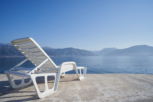 Plastic beach chair against sea and mountains, travel concept.