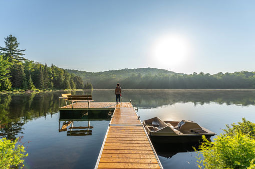 A woman relaxing by a small and quiet fishing lake in the Laurentides (Laurentians), Quebec, during a sunrise of summer.
