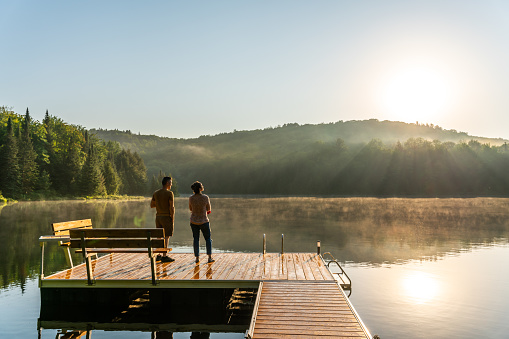 A couple relaxing by a small and quiet fishing lake in the Laurentides (Laurentians), Quebec, during a sunrise of summer.