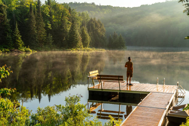 A man relaxing by a small and quiet fishing lake in the Laurentides (Laurentians), Quebec, during a sunrise of summer.