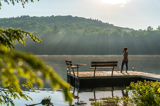 A woman relaxing by a small and quiet fishing lake in the Laurentides (Laurentians), Quebec, during a sunrise of summer.