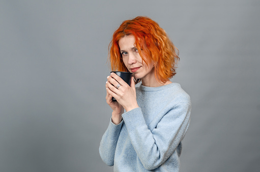 Portrait of cute red-haired woman in casual clothes with drink in her hands. Looking at camera.