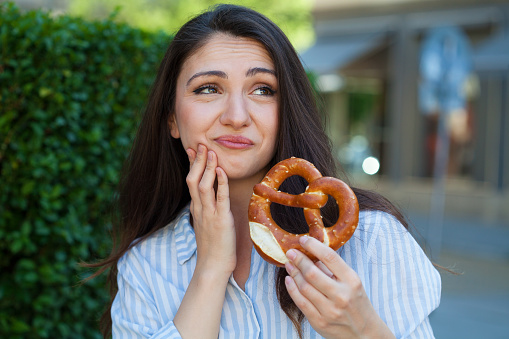 Young woman with a pretzel in hand having toothache