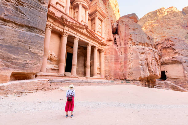 joven viajera con sombrero de pie en el mirador de la antigua ciudad de petra mirando el tesoro o al-khazneh, famoso destino de viaje de jordania y una de las siete maravillas. patrimonio de la humanidad por la unesco. - siq al barid fotografías e imágenes de stock