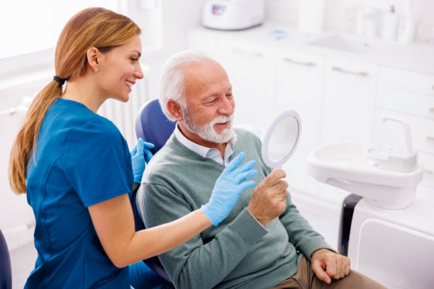 Senior man looking at the mirror at dentist office and smiling Senior man looking at the mirror and smiling after checkup at dentist office; dentist and patient at dental clinic dental hygienist stock pictures, royalty-free photos & images