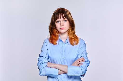 Studio portrait of serious sad young woman looking at camera on light background. Teenage unhappy red-haired female student, emotions, youth, mood, lifestyle, young people concept