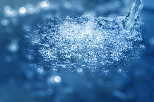 close up of a cool water jet in a sparkling water surface from above, abstract fresh water background with fizzy bubbles in blue and white colors
