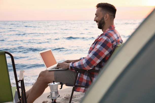 istock Man using laptop in camping chair on sandy beach 1397223247