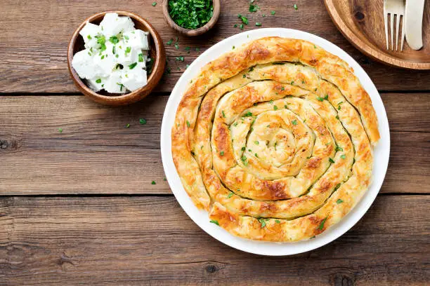 Traditional feta cheese phyllo pastry pie on wooden background .