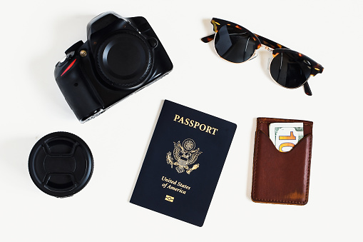 A flat lay shot of a passport, camera, wallet and sunglasses