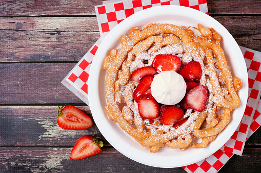 Strawberry funnel cake top view over a dark wood background. Traditional summer carnival treat.