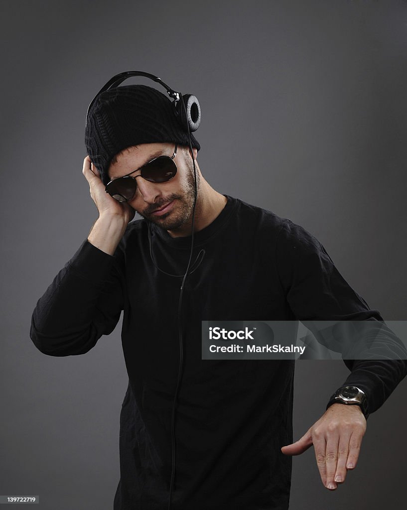 DJ with headphones DJ listening to headphones on a dark background.  His hand is out as he is about to spin a record. Adult Stock Photo