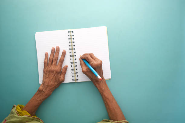 vista superior de la mano de la mujer mayor sobre papel en blanco sobre la mesa - diary writing women human hand fotografías e imágenes de stock