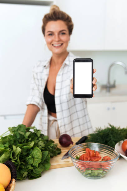 istock Woman is holding smartphone with blank screen for your design during cooking in modern kitchen 1397232565