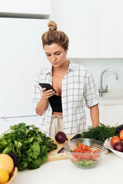 istock Woman with wireless earbuds is using smartphone during cooking in modern white kitchen 1397232636