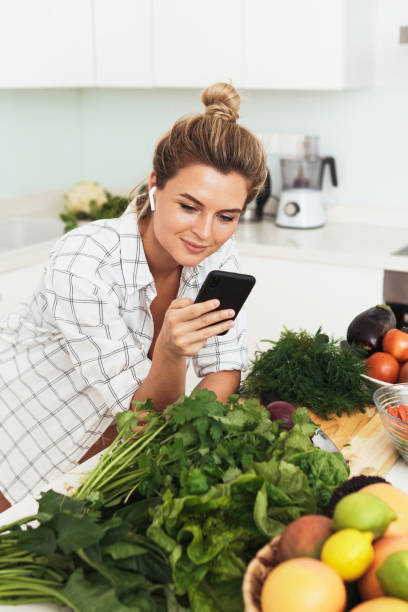 istock Woman with wireless earbuds is using smartphone during cooking in modern white kitchen 1397232647