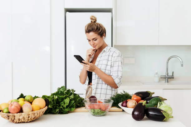 istock Woman with wireless earbuds is using smartphone during cooking in modern white kitchen 1397232667