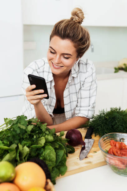 istock Woman with wireless earbuds is using smartphone during cooking in modern white kitchen 1397232710