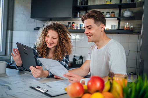 Cheerful young couple managing house finances in the kitchen