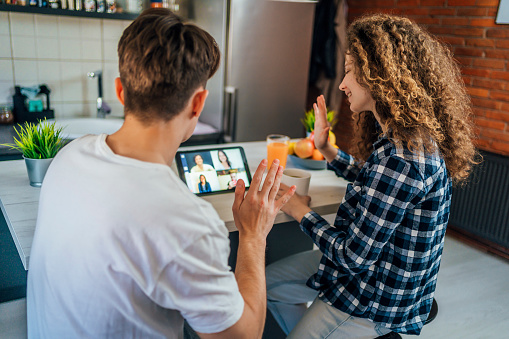 Young couple talking on video call with friends on tablet in the kitchen at home