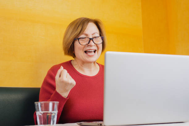 взволнованная пожилая женщина смотрит на экран компьютера триумфом выигрыша в лотерею онлайн. чувствуя эйфорию, читайте хорошие новости о  - new opportunities audio стоковые фото и изображения