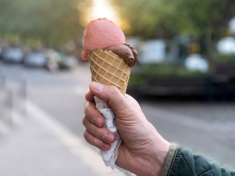 Summer ice-cream season, male hand holding waffle cone with two colorful scoops of ice cream