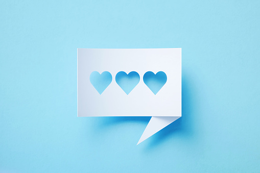Rectangular shaped white chat bubble with cutout three heart shapes sitting on blue background. Horizontal composition with copy space. Social media concept.