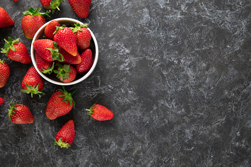 Fresh strawberries in a bowl on black colored wooden kitchen table