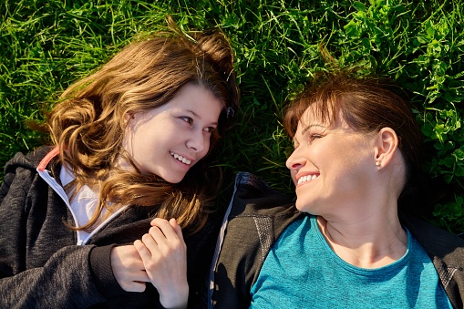 Top view of mother and daughter 11, 12 years old lying together on grass. Happy faces of mother and girl, smiling parent and child. Family, happiness, leisure, lifestyle, love, mother's day concept