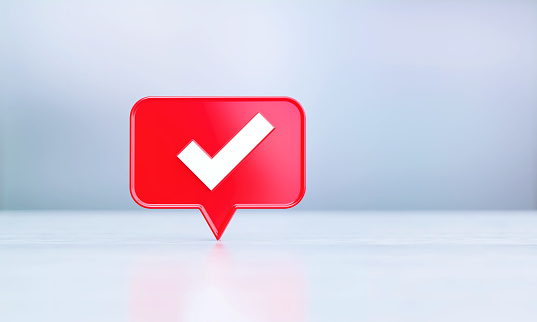 Red speech bubble with white check mark sitting on silver reflective surface before silver defocused background. Horizontal composition with copy space.