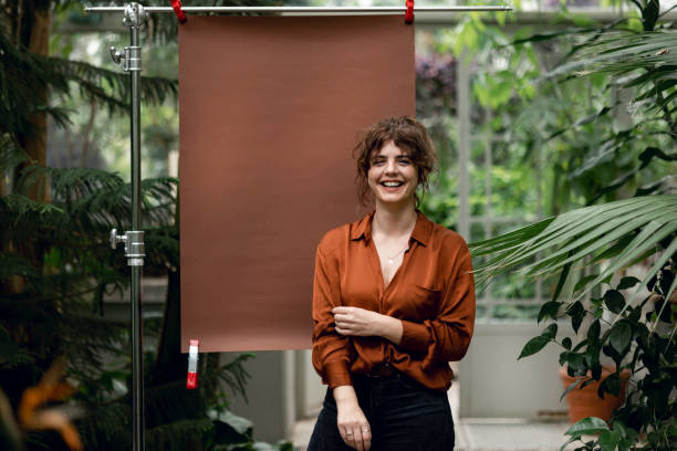 Happy young woman in a botanical garden Portrait of a beautiful happy woman standing in a botanical garden with a brown colour backdrop setup behind her, looking at the camera photo studio model stock pictures, royalty-free photos & images